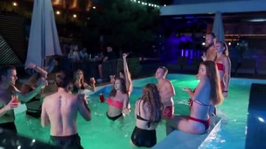 Arkadaşların özel villa havuzunda gece havuzu partisi var. Mayo giymiş neşeli genç insanlar su sıçratıyor, dans ediyor ve lüks otellerde parti yapıyorlar. Mutlu erkekler ve kadınlar birlikte takılıyor. Yavaş çekim.