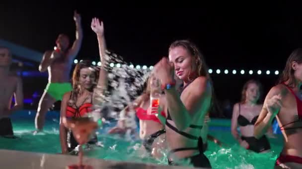穿着比基尼的漂亮女人在晚上的泳池派对上喝着鸡尾酒 和朋友们在一起 在豪华的私人别墅游泳池里 人们一边跳舞一边喝酒和泼水 玩得很开心 慢一点 — 图库视频影像