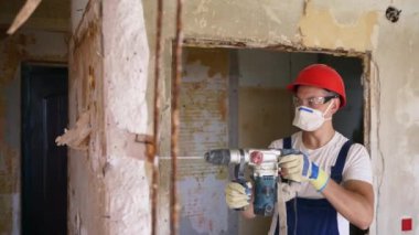 Döner çekiç matkabıyla çalışan bir inşaatçı. Müteahhit, apartman tadilatı ve yenileme için duvarı delmek üzere beton matkapla delik açıyor. Üniformalı elektrikçi elektrik tesisatı kuruyor.