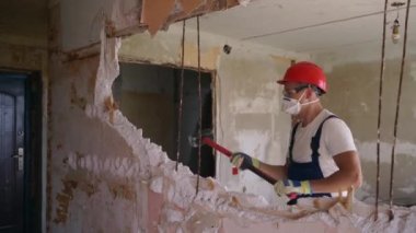 Adam elle sökme ve yıkım işleriyle uğraşıyor. Dairenin tadilatı için büyük çekiçle vuruyor. Müteahhit balyozla duvarı yıkar ve yeniden düzenleme için delik açar. Üniformalı inşaat işçisi.