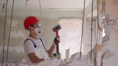 Adam elle sökme ve yıkım işleriyle uğraşıyor. Dairenin tadilatı için büyük çekiçle vuruyor. Müteahhit balyozla duvarı yıkar ve yeniden düzenleme için delik açar. Üniformalı inşaat işçisi.