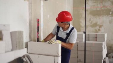 Duvardaki beton blokları kontrol etmek için ruh balonu ve lazer seviyesi kullanıyor. Müteahhit tuğla işi için aletler kullanır. İşçi yeni apartman dairesine duvar örüyor..