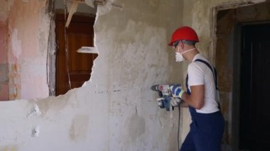 Döner çekiç matkabıyla çalışan bir inşaatçı. Müteahhit, apartman tadilatı ve yenileme için duvarı delmek üzere beton matkapla delik açıyor. Parçalamak ve yıkmak işe yarıyor..