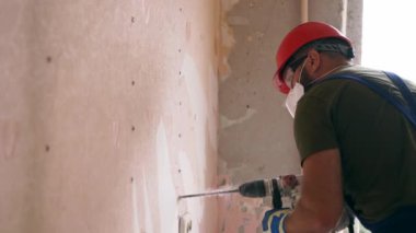 Döner çekiç matkabıyla çalışan bir inşaatçı. Müteahhit, apartman tadilatı ve yenileme için duvarı delmek üzere beton matkapla delik açıyor. Üniformalı elektrikçi elektrik tesisatı kuruyor.