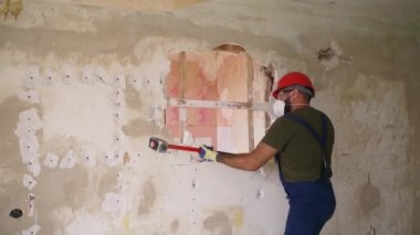 Adam elle sökme ve yıkım işleriyle uğraşıyor. Dairenin tadilatı için büyük çekiçle vuruyor. Müteahhit balyozla duvarı yıkar ve yeniden düzenleme için delik açar. Üniformalı inşaat işçisi.