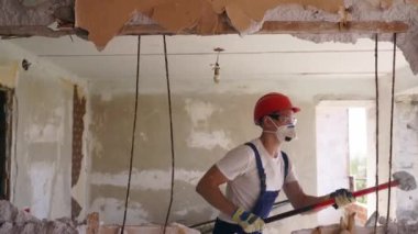 Adam elle sökme ve yıkım işleriyle uğraşıyor. Dairenin tadilatı için büyük çekiçle vuruyor. Müteahhit balyozla duvarı yıkar ve yeniden düzenleme için delik açar. Üniformalı inşaat işçisi.