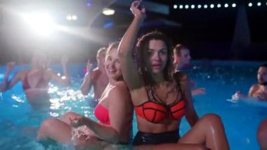 Arkadaşların özel villa havuzunda gece havuzu partisi var. Mayo giymiş neşeli genç insanlar su sıçratıyor, dans ediyor ve lüks otellerde parti yapıyorlar. Mutlu erkekler ve kadınlar birlikte takılıyor. Yavaş çekim.