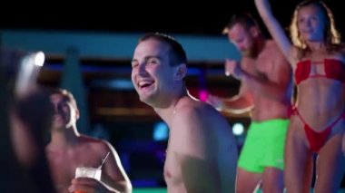 Arkadaşların özel villa havuzunda gece havuzu partisi var. Mayo giymiş neşeli genç insanlar su sıçratıyor, dans ediyor ve lüks otellerde parti yapıyorlar. Mutlu erkekler ve kadınlar birlikte takılıyor. Yavaş çekim.