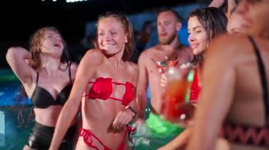 Arkadaşların özel villa havuzunda gece havuzu partisi var. Mayo giymiş neşeli genç insanlar su sıçratıyor, dans ediyor ve lüks otellerde parti yapıyorlar. Mutlu erkekler ve kadınlar birlikte takılıyor. Yavaş çekim.