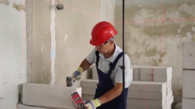 Tuğla ustası lastik çekiç kullanarak beton blokları yıkıyor. Müteahhit, tuğla işi için kesin ruh balonu ve lazer seviyesi kullanır. İşçi yeni apartman dairesine duvar örüyor..