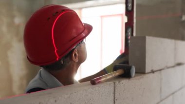 Tuğla ustası lastik çekiç kullanarak beton blokları yıkıyor. Müteahhit, tuğla işi için kesin ruh balonu ve lazer seviyesi kullanır. İşçi yeni apartman dairesine duvar örüyor..