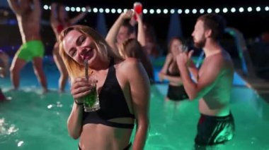 Bikinili güzel bir kadın kokteyl içiyor ve gece havuzu partisinde arkadaşlarıyla takılıyor. İnsanlar lüks bir özel yüzme havuzunda içkilerle dans edip su sıçratarak eğleniyorlar. Yavaş