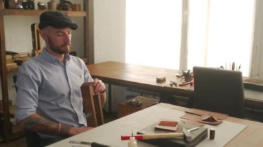 Deri ustası bir atölyede çalışıyor. Usta deri cüzdan yapıyor. Adam deri işi için kontrplak dikişli midilli ya da tahta mengene kullanıyor. Atölyede elinde iğne ve iplik olan bir adam..