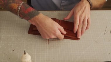 Deri ustası bir atölyede çalışıyor. Usta deri cüzdan yapıyor. Adam yapıştırıcı yapıştırır ve yapıştırır. Cüzdan parçaları kart tutucu ve bozuk para cep ile birleştirir..