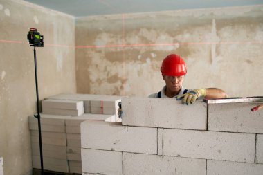 Duvardaki beton blokları kontrol etmek için ruh balonu ve lazer seviyesi kullanıyor. Müteahhit tuğla işi için aletler kullanır. İşçi yeni apartman dairesine duvar örüyor..