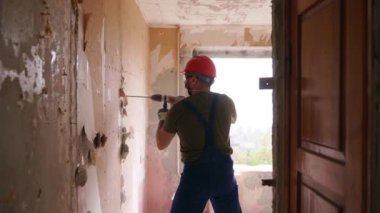 Döner çekiç matkabıyla çalışan bir inşaatçı. Müteahhit, apartman tadilatı ve yenileme için duvarı delmek üzere beton matkapla delik açıyor. Üniformalı elektrikçi elektrik tesisatı kuruyor.