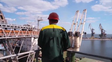 Deniz limanı işçisi buğdayı deniz tahıl asansöründeki kargo konteynırına yüklemeye bakıyor. Tahıl sevkiyatı silolardan toplu taşımacılığa taşınıyor. Tarım ürünlerinin nakliyesi.