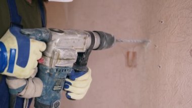 Döner çekiç matkabıyla çalışan bir inşaatçı. Müteahhit, apartman tadilatı ve yenileme için duvarı delmek üzere beton matkapla delik açıyor. Üniformalı elektrikçi elektrik tesisatı kuruyor.