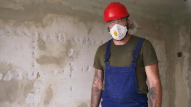 Müteahhit ayakta duruyor, daire dekorasyonunda el yapımı döner çekiç matkabını kaldırıyor. Koruyucu gözlüklü, şapkalı, tulumlu, düşük açılı kahraman pozu için kameraya bakan inşaat işçisi..