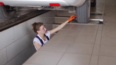 Kadın tamirci uzaktan kumandalı hidrolik tekerlek oyun dedektöründe araba süspansiyonunu inceliyor. Tulum giymiş güçlü bir kadın koşu takımlarında yıpranmak ve direksiyon başında direksiyon başına geçmek istiyor.