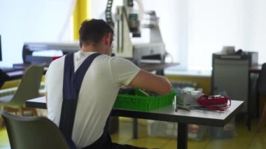 Elektrikçi, elektrik paneli sigorta kutusunu atölyede monte ediyor. İşçi masadaki dağıtım panosuna enerji sayacı, şalterler ve devre kesiciler yerleştirir.