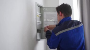 Elektrikçi bir elektrik sigorta kutusunu söküyor. Üniformalı usta elektrik panelinin vidalarını tornavidayla söküp elektriği tamir ediyor. Tamirci ev içi sorunları düzeltiyor.