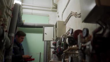 Elektrikçi, bölgedeki ısıtma istasyonunun çoklu sayacıyla kontrol panelini inceliyor. Üniformalı usta elektriği tamir etmek için sigorta kutusunu test sondalarıyla kontrol ediyor. Teknik odada çalışan adam..