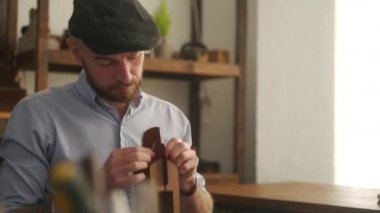 Deri ustası bir atölyede çalışıyor. Usta deri cüzdan yapıyor. Adam deri işi için kontrplak dikişli midilli ya da tahta mengene kullanıyor. Atölyede elinde iğne ve iplik olan bir adam..