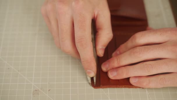 革職人は工房で働く マスター作る二つ折り革財布 ステッチスクラッチ溝を使用して男 男溝革でマーキングツール — ストック動画