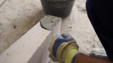 Tuğla ustası otoklava kaplı beton bloklara mala ve spatulayla yapıştırıcı sürüyor. Tuğla işçiliği müteahhidi, inşaat alanında inşaat yaparken köpük betona havan topu koydu..