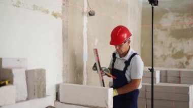 Duvardaki beton blokları kontrol etmek için ruh balonu ve lazer seviyesi kullanıyor. Müteahhit tuğla işi için aletler kullanır. İşçi yeni apartman dairesine duvar örüyor..