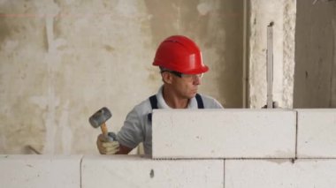 Tuğla ustası lastik çekiç kullanarak beton blokları yıkıyor. Müteahhit, tuğla işi için kesin ruh balonu ve lazer seviyesi kullanır. İşçi yeni apartman dairesine duvar örüyor..