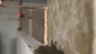 Müteahhit, beton duvara tabancayla poliüretan köpük yapıştırıcı sürerek otomatik kaplamalı beton tuğlayı yapıştırıyor. İşçi PU köpüğü püskürtür. İzole görünüm.