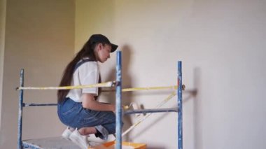 Profesyonel ressam kadın, inşaat alanındaki iskelede paten kayarak duvarı boyuyor. Tulumlu genç bir kadın ev dekorasyonu yapıyor, sahne dekorasyonu yapıyor. İşçi odada DIY onarımı yapıyor.