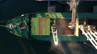 Yukarıdaki hava manzarası - buğday deniz limanındaki deniz tahıl asansöründe yük ambarına yükleniyor. Buğday sevkiyatı ambardan gemiye deniz limanı terminalindeki sandıkla taşınıyor. Deniz taşımacılığı.