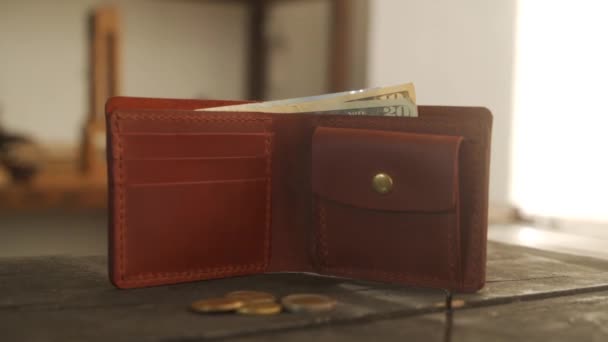 コインポケットとカードホルダーと現金とブラウン二つ折りの財布は革のワークショップで暗い木製のテーブルの上にあります ポーチ ドルおよびユーロノート コピースペースのコイン 経済の概念 — ストック動画