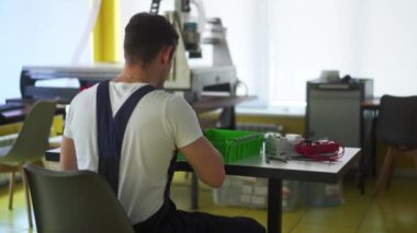 Elektrikçi, elektrik paneli sigorta kutusunu atölyede monte ediyor. İşçi masadaki dağıtım panosuna enerji sayacı, şalterler ve devre kesiciler yerleştirir.