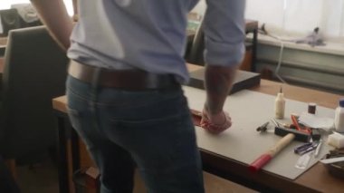 Deri ustası bir atölyede çalışıyor. Usta çift katlı deri cüzdan yapıyor. Adam kazı kazan kullanıyor. Adam işaretleme aracı ile deri yiv.
