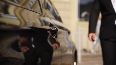 Siyah takım elbiseli şoför arabanın kapı kolunu açar. İş adamı araca biniyor. Alıcı yeni arabayı dener ve sürücü koltuğuna oturur..