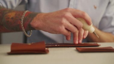 Deri ustası atölyesinde çalışıyor. Usta deri cüzdan yapıyor. Erkekler deri şekilli kenarlara yapıştırıcı sürerler..