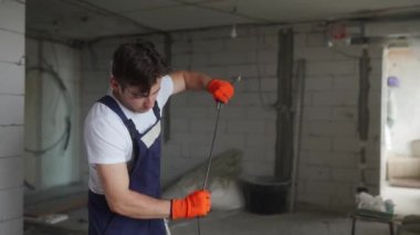 Elektrikçi kabloları döşeyip, eve elektrik kabloları yerleştiriyor. Tulum ve eldiven giyen inşaatçı inşaat alanına elektrik kabloları yerleştiriyor. Adam apartman tadilatı yapıyor..