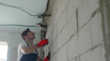 Elektrikçi bağlantı kutusunu bağlıyor, daireye elektrik kabloları yerleştiriyor. Tamirci kabloları besliyor, kabloyu elektrik kutusuna bağlıyor. Müteahhit apartman tadilatında çalışıyor. Tamir ve inşaat işleri.
