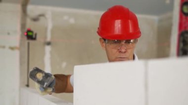 Tuğla ustası lastik çekiç kullanarak beton blokları yıkıyor. Müteahhit, tuğla işi için kesin ruh balonu ve lazer seviyesi kullanır. İşçi yeni apartman dairesine duvar örüyor..