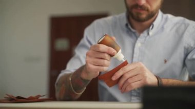 Deri ustası bir atölyede çalışıyor. Usta deri cüzdan yapıyor. Erkekler deri şekilli kenarlara yapıştırıcı sürerler..