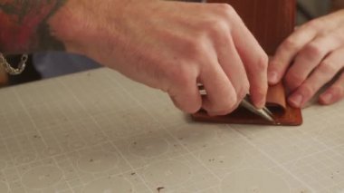 Deri ustası bir atölyede çalışıyor. Usta çift katlı deri cüzdan yapıyor. Adam kazı kazan kullanıyor. Adam işaretleme aracı ile deri yiv.
