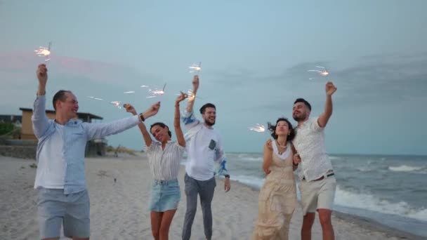 7月4日 多民族朋友们手握彩灯散步 在海滨的晚会上玩得很开心 新年或圣诞节期间 年轻人在海滩上燃放焰火 — 图库视频影像