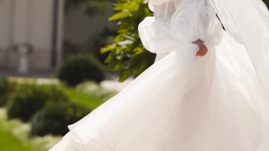 Uzun, havadar peçeli güzel bir gelin, lüks bir saray bahçesinde düğün günü havada uçuşan kumaşla dönen zarif beyaz bir elbise. Çekici, çekici bir kadın kameraya poz veriyor, muhteşem bir elbise içinde..