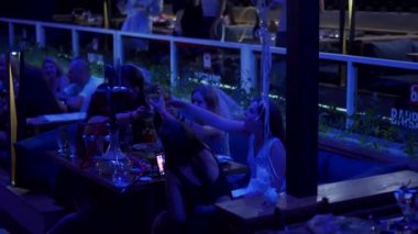 Mariupol, Ukraine - 25 July 2021. Beautiful girls clink glasses of champagne at a bachelorette party in a night club with hookah on a table. Women in wedding veils celebrating clinking glasses.