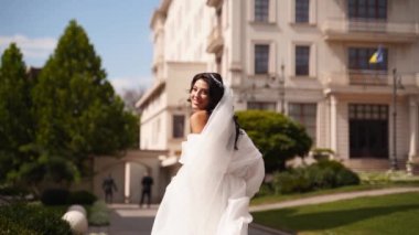 Uzun havadar peçeli, şık beyaz elbiseli güzel gelin düğün günü kameradan kaçıyor. Çekici, oyuncu bir kadın kaçıyor. Arkasını dönüyor, izleyiciye bakıyor. Havada çırpınan kumaş. Beni takip et..