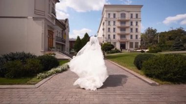 Uzun havadar peçeli, şık beyaz elbiseli güzel gelin düğün günü kameradan kaçıyor. Çekici, oyuncu bir kadın kaçıyor. Arkasını dönüyor, izleyiciye bakıyor. Havada çırpınan kumaş. Beni takip et..